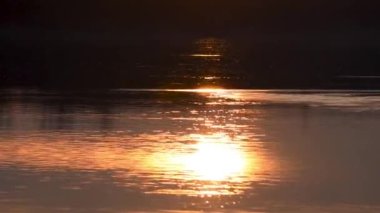 Güneş ışınları dalgalı su yüzeyine yansıyor.