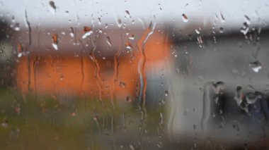 Yağmur yağarken pencere camını kapatın. Arkaplanda su izleri ve bulanık evler olsun.