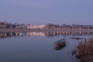 Alacakaranlıkta Sava nehrinin manzarası, su üzerinde yüzen kulübeler ve kıyıda tekne, Hırvatistan 'ın Slavonski Brod kasabası diğer kıyılarda