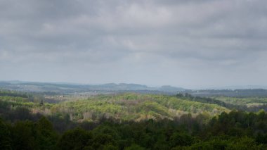 Dağlık kırsal arazi ormanla kaplıydı, kırsal kesimde sabah, uzak mesafede sis ve bulutlu gökyüzü.