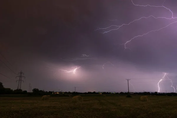 Thunderstorm above field with roll bales at night, lightning in clouds at night in countryside, cloud to cloud branched lightning