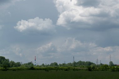 Large clouds over pasture and parts of an oil refinery, cloudy day