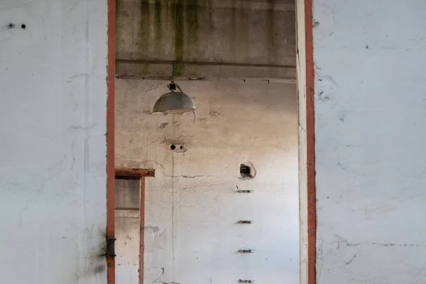 Ceiling light in abandoned industrial building close up through opening in wall, urban exploration