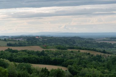 İlkbaharda ormanları ve ekilebilir tarlaları olan kırsal alan bulutlu bir günde, kiliseli tepelik bir köy.