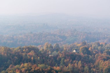 Tepedeki yalnız ev sonbahar renklerinde gür ormanlarla çevrili, uzak tepeler sabah sisinde kayboluyor.