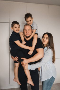 İki oğlu olan sevgi dolu bir ailenin portresi. Dört kişilik mutlu bir beyaz aile. Hamile kadın kocasını ve oğullarını kucaklıyor. Oğullar babanın kollarında. Seçici odak