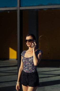 Havalı kız Tel 'de konuşuyor. Mağaza vitrininin yanında kısa şortlu güzel bir kız..