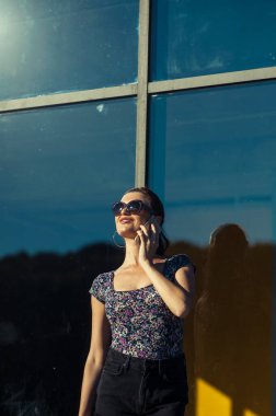 Havalı kız Tel 'de konuşuyor. Mağaza vitrininin yanında kısa şortlu güzel bir kız..