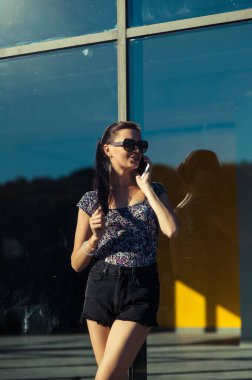 Havalı kız Tel 'de konuşuyor. Mağaza vitrininin yanında kısa şortlu güzel bir kız..