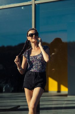 Havalı kız Tel 'de konuşuyor. Mağaza vitrininin yanında kısa şortlu güzel bir kız..