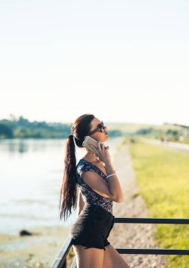 Çekici hippi kız açık havada iskelede 4G bağlantısı olan yeni cep telefonuyla postaları kontrol ediyor, pozitif kadının nehir kenarında dinlenirken modern cep telefonundan mesaj gönderdiğini görüyor..