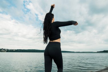 Spor kıyafetleri içinde gün batımına karşı spor egzersizleri yapan çekici bir kadın. Aktif genç kız