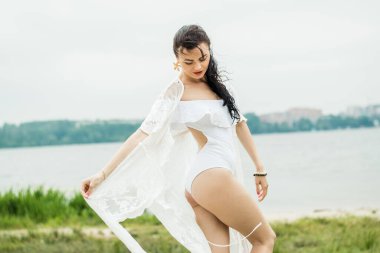 Plajda şeffaf beyaz elbiseli bir kız. Beyaz mayolu mutlu bir kız. Kız sahilde yürüyor..