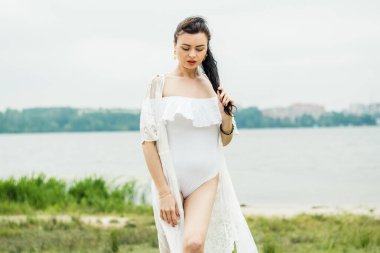 Plajda şeffaf beyaz elbiseli bir kız. Beyaz mayolu mutlu bir kız. Kız sahilde yürüyor..