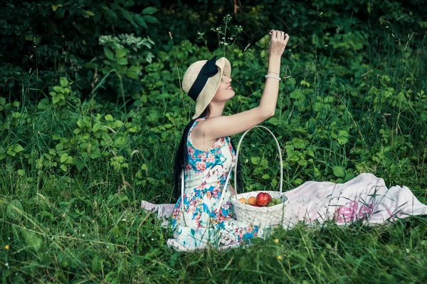 庭にリンゴを持つ女性 熟れた赤と緑のリンゴの完全なバスケットを持つ若い魅力的な女性は リンゴの庭の芝生の上に横たわって笑顔です 収穫期だ 田舎暮らし — ストック写真