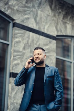 İş adamı telefonda, bir toplantıda konuşuyor. Adam el sallıyor. Yakışıklı, esmer, sakallı, gülümseyen yönetici. İş yerinde çalışıyor, telefonda konuşuyor.