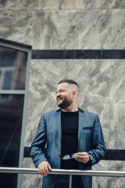 Ofisin yakınında bir adam toplantı bekliyor. Mavi takım elbiseli bir iş adamı..