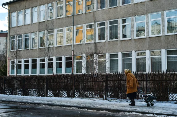 Tekerlekli çanta taşıyan yaşlı bir kadın hastane yakınlarında yalnız başına yürüyor, yalnız bir emekli, kovid19, temiz havada yürüyor, Ivano-Frankivsk, Ukrayna, 21 Ocak 2021