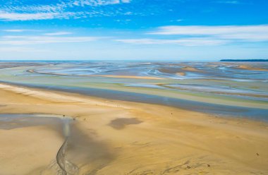 Kuzey Fransa, Normandiya 'da alçak gelgit sırasında Le Mont Saint Michel' i çevreleyen renkli kum düzlüklerinde yürüyen turistler