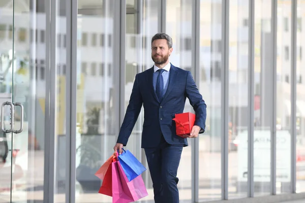 Πλούσιος. Επιχειρηματίας ψωνίζει σε ένα εμπορικό κέντρο. Ευτυχισμένος επιχειρηματίας με κοστούμι που κρατάει χαρτοσακούλες. Shopaholic άνθρωπος με τα πόδια σε εμπορικό δρόμο με πολλές τσάντες ψώνια. — Φωτογραφία Αρχείου