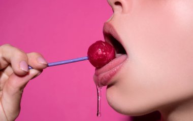 Orgazm konsepti. Kadın ağzında lolipop, kırmızı ruj. Kırmızı, parlak bir lolipopu yalayan bir kadın. Kapatın. Seksi ağzında lolipopla seksi bir kadın..