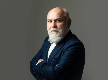 Kollarını kavuşturmuş kıdemli adam. Belden yukarı portre. Sakallı, orta yaşlı, ciddi bir yüz ifadesi olan, yakın plan bir kafa ve omuz portresi olan adam..