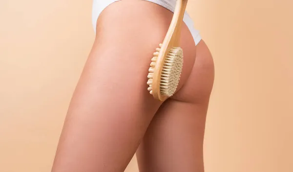 Woman legs with clean skin. Female buttocks ass without cellulite. Brushing skin buttocks and butt with a dry wooden brush to prevent and treatment cellulite and body problem. — Stockfoto