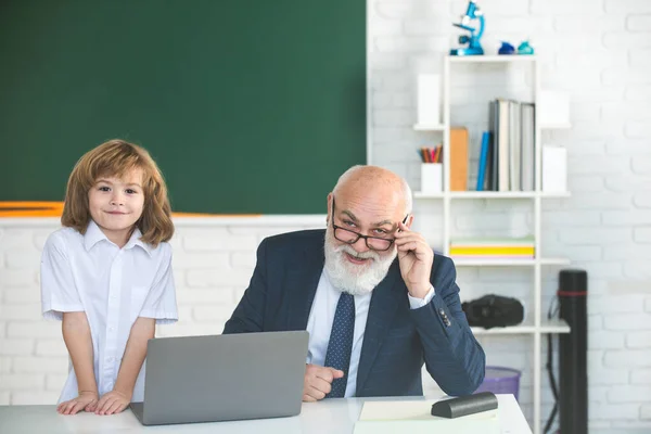 Online oktatás. Régi tanár és diák az iskolában. Iskolásfiú az osztályteremben laptop. — Stock Fotó