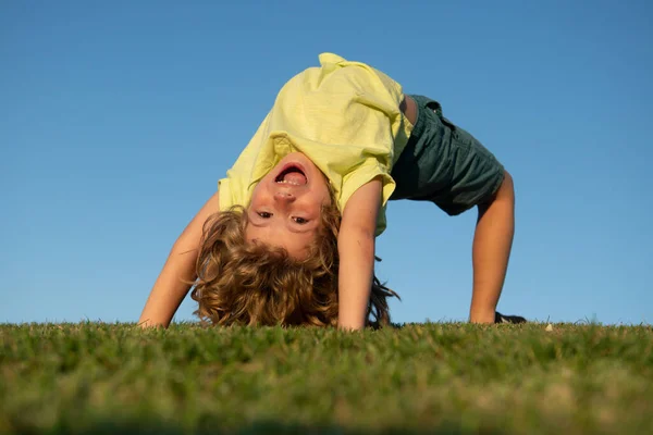 Bambino ragazzo a testa in giù all'aperto nella soleggiata giornata estiva. Bambino felice sdraiato sull'erba verde. Ragazzo divertente all'aperto nel giardino primaverile. Giornata della Terra e concetto di stile di vita sano. — Foto Stock