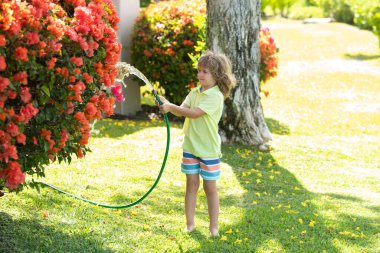 Mutlu çocuk hortumdan su döküyor. Amerikalı çocukların çocukluğu. Bahçede çiçekleri sulayan çocuk. Evde bahçe işleri..