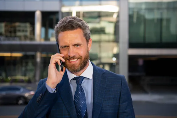 Бизнесмен разговаривает по телефону. Портрет веселого офисного работника, разговаривающего по мобильному телефону рядом с современным офисом. — стоковое фото