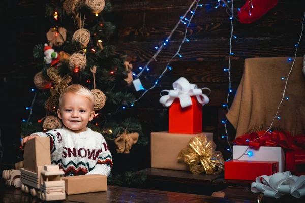 Frohe Weihnachten. Portrait Kind mit Geschenk auf Holzgrund. Lächelndes Kind, das hinter dem Weihnachtsbaum im Wohnzimmer hervorlugt. Christbaumschmuck. Glückliche Kinder. — Stockfoto