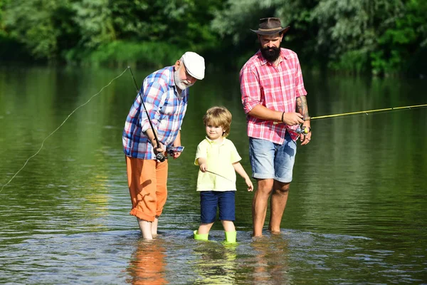 Little boy on a lake with his father and grandfather. Great-grandfather and great-grandson. Father teaching his son fishing against view of river and landscape. — Stock Photo, Image