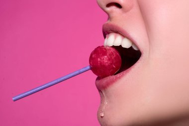 Ağzında kırmızı lolipop şekeri tutan pembe rujlu yakın plan kadın dudakları. Lolipop dudaklı kadın yüzü.