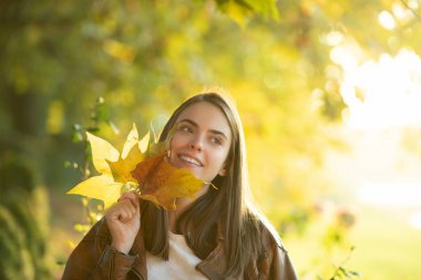 Güzel kadın yüzünün yanında sarı yapraklar tutuyor..