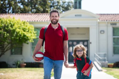 Baba oğluna okula kadar eşlik ediyor. Sırt çantalı ilkokul öğrencisinin ebeveyni ve öğrencisi..