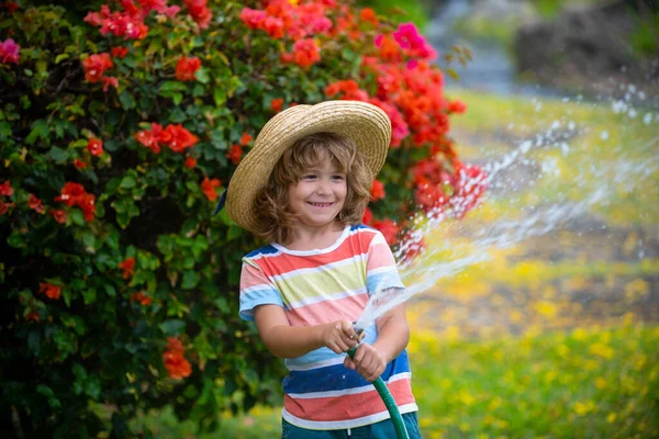 Забавный мальчик играет со шлангом на заднем дворе. Ребенок веселится с брызгами воды. Активный отдых на природе для детей. — стоковое фото