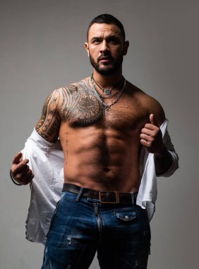 Dövmeli, vahşi, yakışıklı bir adam. Erkekler sıradan dövmeler yaptırır. Acımasız yakışıklı erkek modelin portresi. Düğmesiz gömlekli kaslı seksi erkek. Seksi, çıplak gövdeli yakışıklı adam..