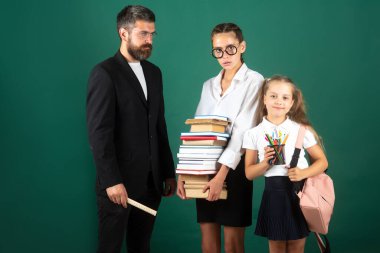 Baba, öğretmen ve okul çocuklarının portresi yeşil karatahta arka planda. Kitap okumak ve yazmak. Babam okulda kız öğrencilere ders veriyor..