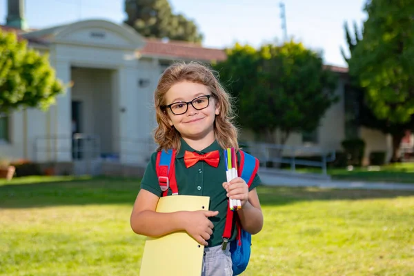 Un pequeño y sonriente libro de mochilas. Retrato de un joven feliz fuera de la escuela primaria. Cara de primer plano de alumno feliz al aire libre. Chico nerd divertido. —  Fotos de Stock