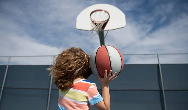 Söt liten pojke håller en korg boll försöker göra en poäng. — Stockfoto