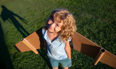 Yaz parkında oyuncak uçak kanatlarıyla oynayan tatlı bir çocuk. Yenilik teknolojisi ve başarı konsepti. Çocuk pilot parkta çimlerde eğleniyor..