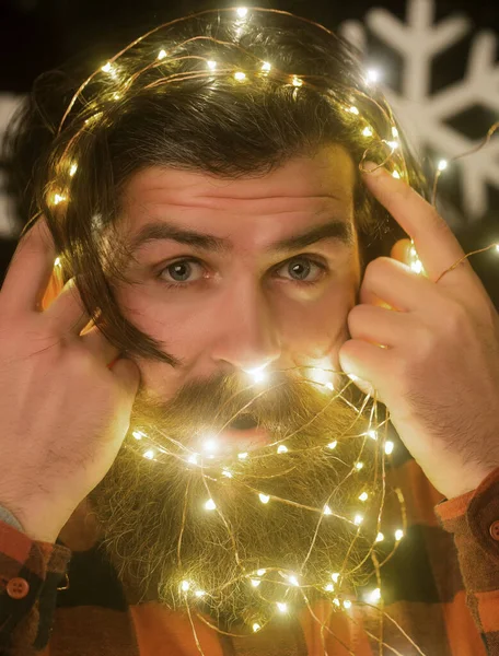 Garland op de kerstman als decoratie. Kerstman met baard op verrast gezicht en bloemenslinger. Nieuwjaar jongen met verlichte draad — Stockfoto