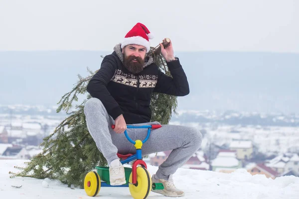 Divertente ciclista in cappello da Babbo Natale e abbigliamento sportivo nella giornata invernale. Hipster che porta l'albero di Natale sulla neve bianca. Triciclo uomo in bicicletta sul paesaggio innevato — Foto Stock