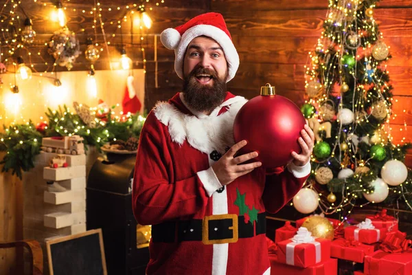 Hipster hombre, barbudo de Santa celebrar el día de Acción de Gracias y la Navidad. Retrato de Papá Noel feliz con pelotas de juguete decorativas cerca del árbol de Navidad . —  Fotos de Stock