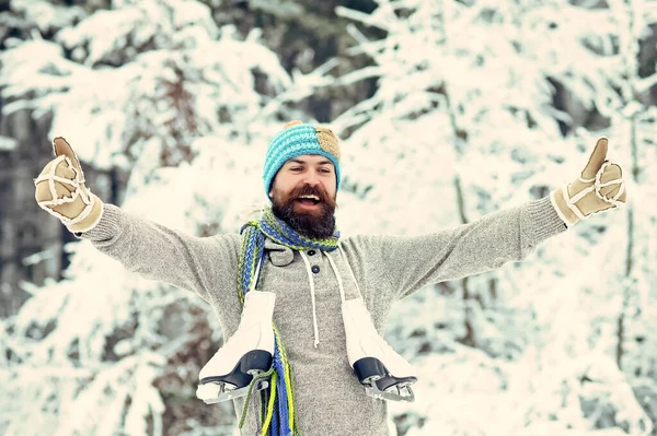 Zimní muž. Vousatý muž se šťastnou tváří drží ruku s bruslí ve zasněženém zimním lese na vánoční prázdniny. Zimní sport a odpočinek — Stock fotografie