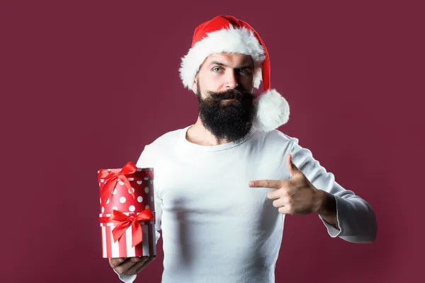 Retrato de un hombre guapo con barba larga y bigote en rojo Santa Claus sombrero de Navidad sosteniendo la caja presente en el estudio sobre fondo púrpura. Santa barbuda —  Fotos de Stock