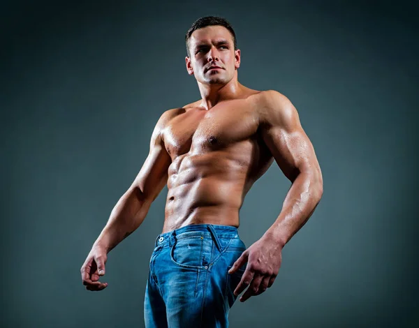 Портрет красивого сексуального м'язистого чоловіка, спортсмена з ідеальним тілом на темному тлі. Сексуальні м'язи сильний хлопець обличчя в джинсах на сірій студії ізольовані . — стокове фото
