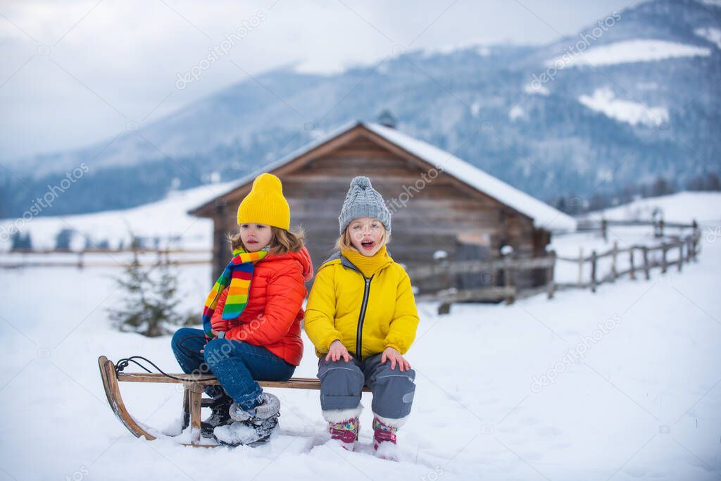 Kids boy and little girl enjoying a sleigh ride. Children sibling together sledding, play outdoors in snow on mountains in winter.