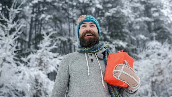 Hipster Santa na floresta fria de inverno nevado. Boas festas e xmas. Homem barbudo em Papai Noel no ano novo. Natal homem feliz com barba segurar caixa de presente — Fotografia de Stock